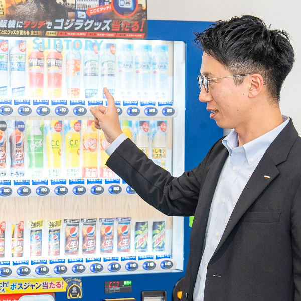 T.I.さんが自動販売機の前で説明している様子