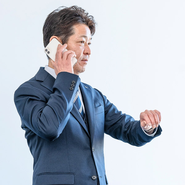 H.S.さんが腕時計を見ながら携帯電話で話している様子